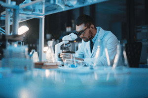 A medical researcher examining a sample under a microscope - DeliveryApp Medical Courier Services