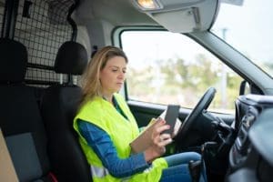 self-employed courier driver jobs - a woman sat in a van wearing a high viz jacket scanning a parcel wither her phone.